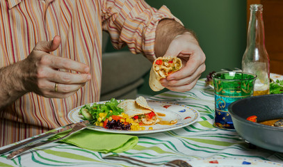 Detail of man hands eating mexican fajitas and salad