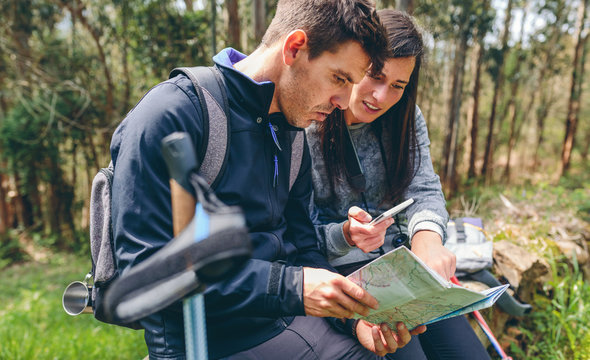 Young couple doing trekking sitting looking mobile and map outdoors