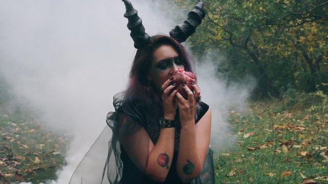 Demoness is eating a heart of human. Black witch with a heart in her hands