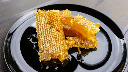 Fragrant summer honey in honeycombs, collected by domestic bees, lies on a table on a black shiny plate, ready for a healthy meal for breakfast