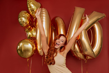 Festive girl in good mood wearing party dress having fun with raised up hands against background with balloons