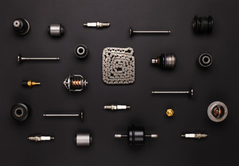 Studio photography - a lot of automotive parts: valves, spark plugs, silent blocks, thermostats, filter, sensors, chain, ball bearings, lie in straight rows on a flat surface isolated on a black 