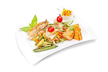 Pieces of fish fillet, fried and served on a white dish, with leaves of mint, cherry tomatoes, an asparagus beans, peppers, zucchini segment. Isolated on white background. 
