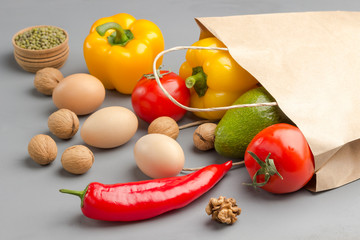 A set of products for healthy eating. Paper bag with walnuts, chickpeas, beans, lentils, yellow and red peppers, tomatoes, avocado on a gray background. .