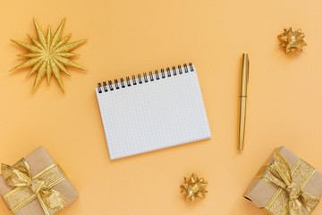 Holiday background, gold background with glitter gold star and gift boxes , open spiral notepad and pen, flat lay, top view, copy space