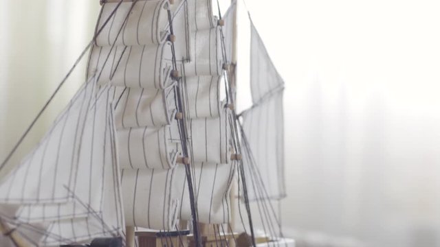 Wooden ship toy model standing on a wooden table in light room, hobby concept. Stock footage. Close up of the sailing ship small figure.