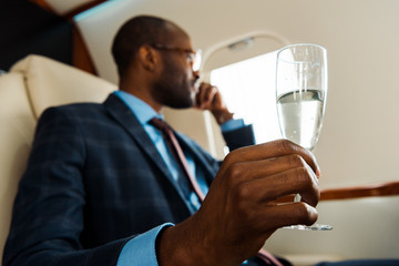 selective focus of african american man holding champagne glass in private plane