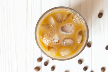 Iced coffee with milk in glass on white wooden background, top view. Close-up glass with drink on table. Summer beverage