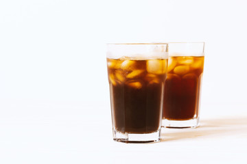 Fototapeta na wymiar Black tea, coffee or cola with ice in glass on white background. Horizontal photo with copy space. Two glass with drink on table. Summer beverage