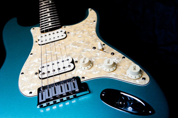 Fototapeta na wymiar A details of a light Blue electric guitar on a black background.