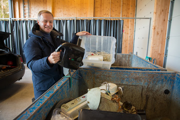 A man putting old appliances into dumpster in sorting centre for safe disposal and recycling