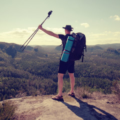 Traveler with backpack and sticks looks on  mountain peak