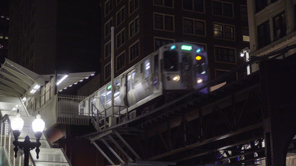 Night time exterior of loop train passing through elevated station on tracks through downtown chicago during dark evening rush hour commute