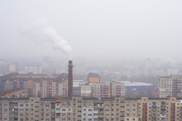 Smoking chimney of a thermal power plant on the background of a snowing city