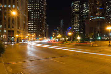 Night time long exposure of generic busy downtown city urban street with car light trails traveling down highway through metropolis intersection, skyline in background