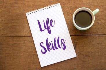 Life skills text on open notebook with coffee cup on wooden table