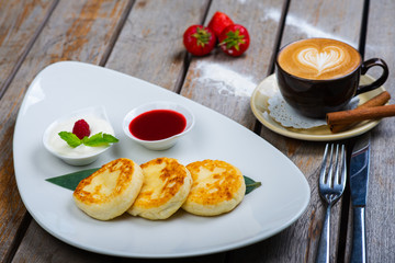 Traditional breakfast with coffee and cheesecakes, cottage cheese pancakes on a plate with syrup and jam.