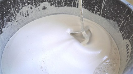 Plasterer knead the solution with a perforator. Workers knead a white solution in a bucket. The mixture for the bulk floor is stirred in a bucket.