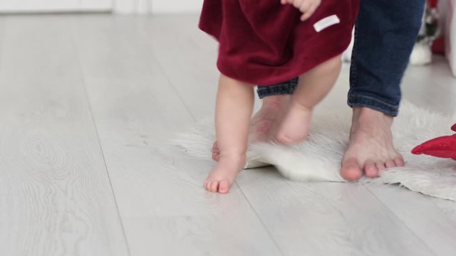 Father holds baby infant toddler teach first steps barefoot feet on home floor parquette