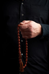 man in a black shirt holds a brown stone rosary in his left hand, low key
