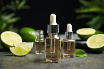 Lime essential oil and cut citrus fruits on grey table