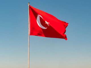 Turkish flag is waving on the top of the flagpole against bright clear blue sky at the background