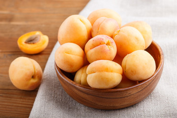 Naklejka na ściany i meble Fresh orange apricots in wooden bowl on wooden background. side view.