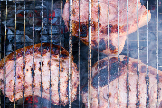 Few pieces of slightly burnt meat on charred grate with coals and smoke below