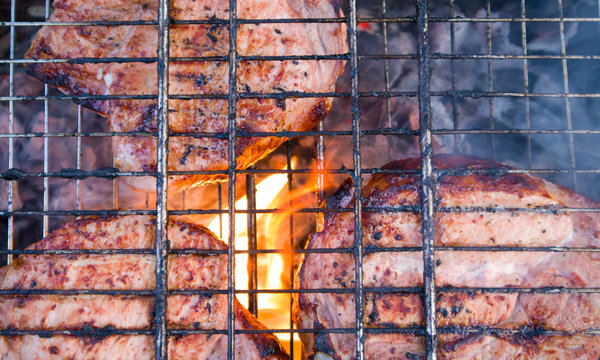 Few pieces of slightly burnt meat on charred grate with fire and smoke below