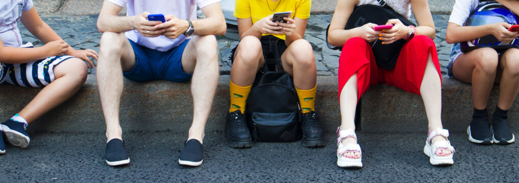 Group of teenagers sitting with phones on the sidewalk 