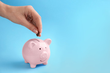 Woman putting coin into piggy bank on light blue background, closeup. Space for text