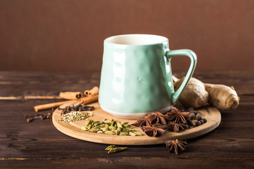Clay cup on a wooden board on a dark background. A cup of masala tea. Spices cloves, fennel, cinnamon, cardamom, milk.