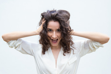 Happy amazed student girl gasping or shouting for joy, holding head. Wavy haired young woman in casual shirt standing isolated over white background. Surprise or joy concept