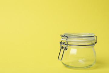 Closed empty glass jar on light yellow background, space for text