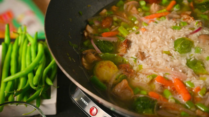 Frying and cooking rice and meat in a wok with vegetables, on a black wooden background, with space. Culinary background, gastronomy, Asian and Oriental cuisine. Thailand