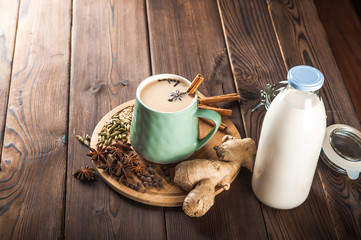 Clay cup on a wooden board on a dark background. A cup of masala tea. Spices cloves, fennel, cinnamon, cardamom, milk.