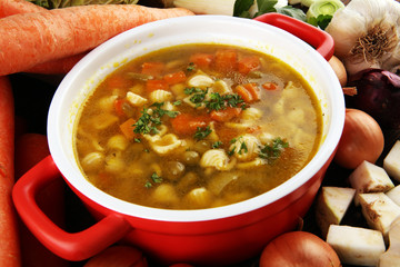 Broth with noodles and carrots, various fresh vegetables in a pot - colorful fresh clear spring...