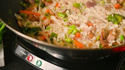 Frying and cooking rice and meat in a wok with vegetables, on a black wooden background, with space. Culinary background, gastronomy, Asian and Oriental cuisine. Thailand