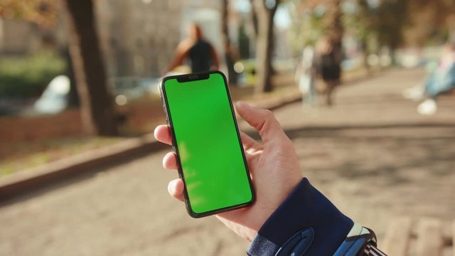 NEW YORK - May 19, 2019: Close up young hand man using phone with vertical green screen background park city blurred internet chrome cellular smartphone scrolling tapping communication slow motion