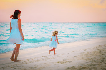 mother and little girl walking on beach at sunset, family vacation