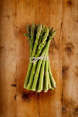 A portrait view of fresh bunch of asparagus, tied with a string bow, shot on a wooden background, with copy space