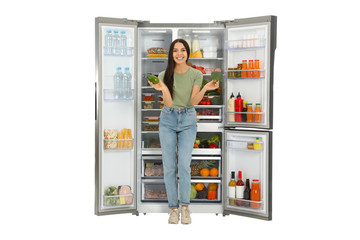 Young woman with broccoli and avocado near open refrigerator on white background
