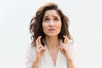Anxious woman keeping fingers crossed and praying for luck. Wavy haired young woman in casual shirt...
