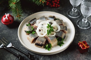 Slices of herring with onions, butter and vinegar on a white dish.