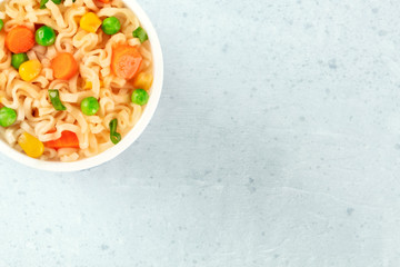 Ramen cup, instant soba noodles in a plastic cup close-up, with green peas, carrot pieces, and scallions, shot from above with a place for text