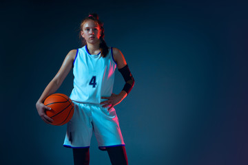 Intensity. Young caucasian female basketball player on blue studio background in neon light, motion...
