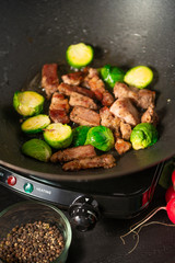 Frying meat with vegetables, on a black wooden background. Cooking, gastronomy. Vertical frame.