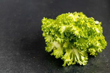 Green lettuce on a dark background. Healthy and healthy food. Can be added to vegetarian salads.