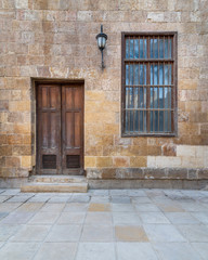 Fototapeta na wymiar Facade of old abandoned stone bricks wall with wooden door and window covered with wrought iron bars and antique lantern, Cairo, Egypt