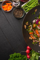 Roasting meat with vegetables, on a black wooden background. Cooking, gastronomy. Vertical frame. Delicious and healthy food, with space for an inscription.